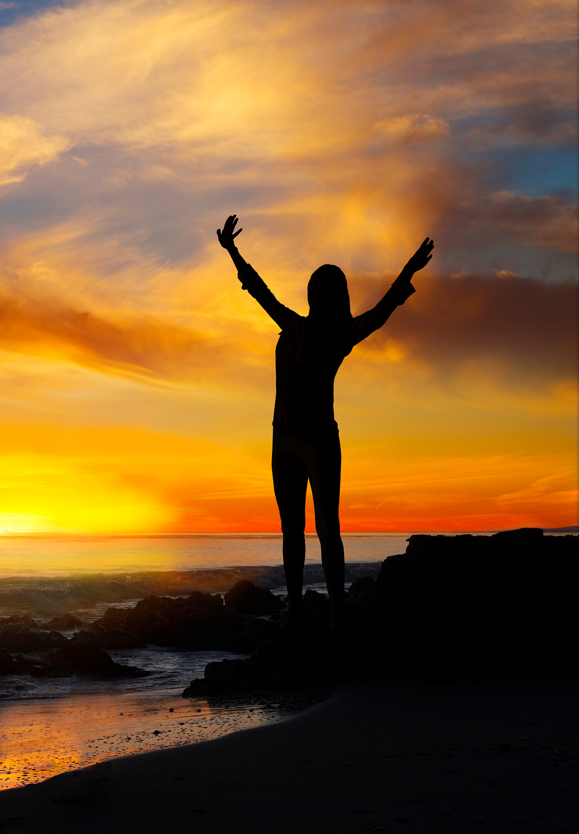 Empowered woman. Woman standing with arms raised near ocean in sunset